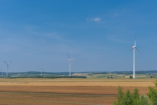 Open landscape with windmill. In the middle of grain fields, electric power lines next to them.