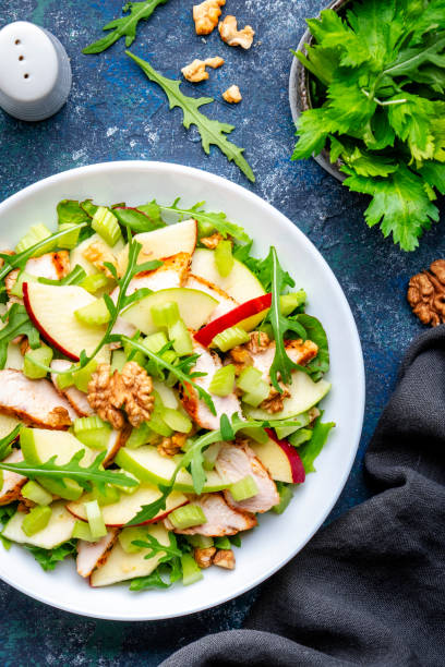 istock Waldorf salad with fresh apple, celery, lettuce, grilled chicken fillet, arugula and walnuts on plate, blue table background, top view 1523383948