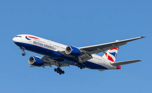 London, England - March 2019: Boeing 777 long haul airliner operated by British Airways taxiing for take off past tail fins of the company's other aircraft.