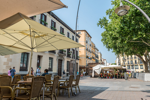 Madrid, Spain - June 27, 2023: View of some neighbors passing through the quiet and traditional square of Tirso de Molina in Madrid. The square has its existence since the year 1840. It is named after Tirso de Molina, a 17th century Spanish playwright who has a statue dedicated to it.