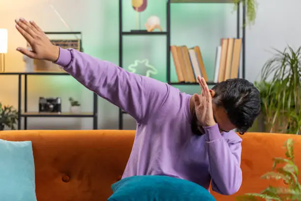 Photo of Trendy cheerful positive indian man dancing and moving to rhythm making dub dance gesture at home