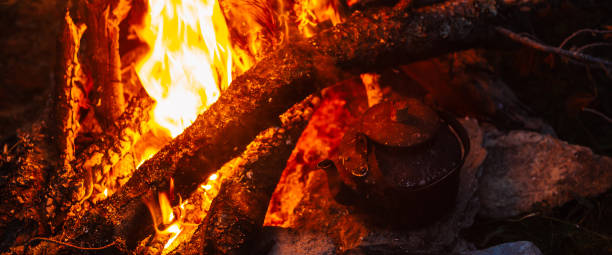 istock Boiling of tea in kettle on bonfire with large firewood. Tea drinking in open air. Active outdoor recreation. Camping in dusk. Romantic warm atmosphere in twilight on nature. Active rest. 1523662814