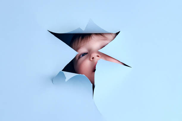 istock Happy baby in a hole on a paper blue background. Torn child head studio background, copy space. Kid aged one year six months 1523665594