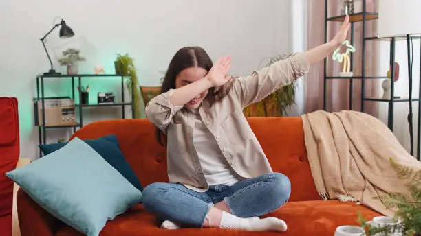 Photo of Trendy cheerful positive woman dancing and moving to rhythm making dub dance gesture at modern home