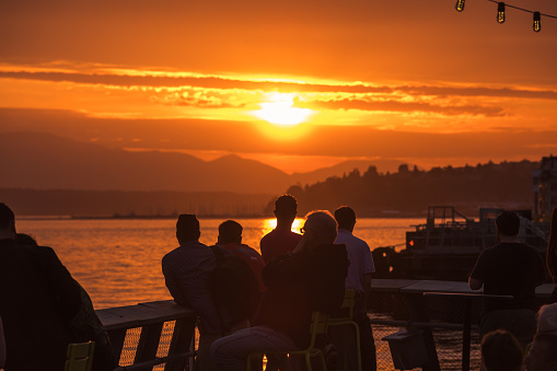 Seattle, USA - Jun 8, 2023: Late in the day a vivid sunset over Elliott bay with people enjoying the view from pier 62.