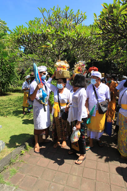 ceremonia balinesa en pura goa lawah o templo de goa lawah en el este de bali con personas vestidas con trajes tradicionales, kebaya, pareos batik y llevando ofrendas en la cabeza y con hombres con sombreros udeng. - pura goa lawah fotografías e imágenes de stock