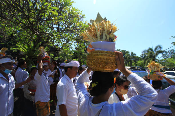 ceremonia balinesa en pura goa lawah o templo de goa lawah en el este de bali con personas vestidas con trajes tradicionales, kebaya, pareos batik y llevando ofrendas en la cabeza y con hombres con sombreros udeng. - pura goa lawah fotografías e imágenes de stock