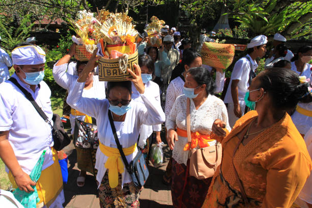 cerimonia balinese al tempio di pura goa lawah o goa lawah nell'est di bali con persone che indossano abiti tradizionali, kebaya, parei batik e portano offerte sulla testa e con uomini che indossano cappelli uden. - pura goa lawah foto e immagini stock