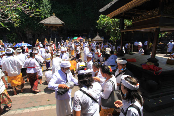 scène à l’intérieur du temple pura goa lawah à klungkung, east bali, indonésie avec de nombreuses personnes vêtues de vêtements traditionnels tels que kebaya et batik sarong avec les hommes portant des couvre-chefs udeng et les femmes avec des fle - pura goa lawah photos et images de collection