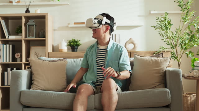 Asian exited male man wear VR or virtual reality glasses,headsets sit relax playing explore new world online at living room in front of TV at home in quarantine period technology and innovation ,A Man excited in virtual reality