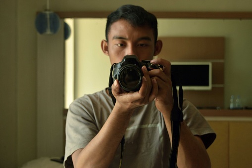 a man holds a DSLR camera in front of a mirror and takes a picture of himself