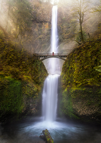 Multnomah Falls view with sunrise and traveller woman standing on the bridge, columbia river gorge, Oregon, USA