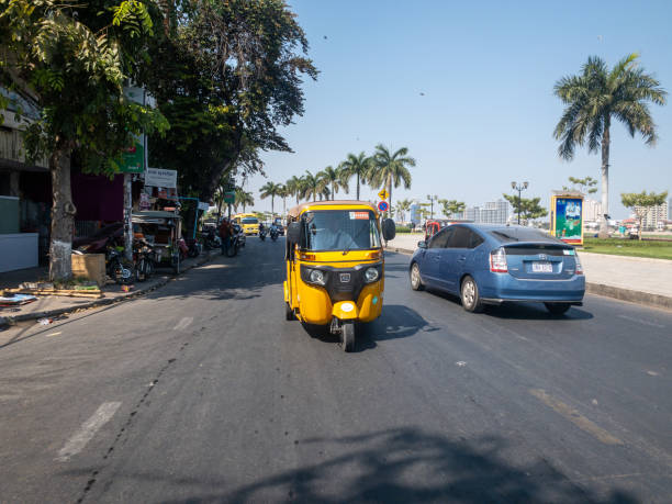 Phnom Penh, Cambodia - 12/26/2019 : A yellow tuk tuk drives on busy road with Pass App sticker
