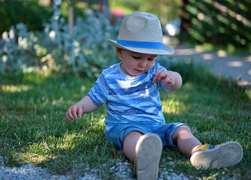 Cute little boy with straw hat sitting on a ground in park