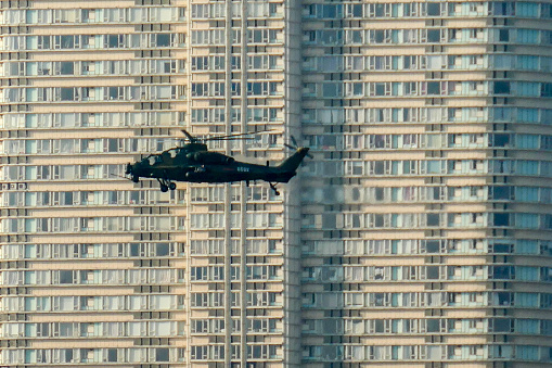 A Changhe Aircraft Industries Corporation (CAIC) Z-10 attack helicopter of the Chinese People's Liberation Army (PLA) Hong Kong Garrison patrolling over Victoria Harbour.  In the background is a residential complex in Kowloon.   This image was taken on a late, sunny afternoon on 7 July 2023.