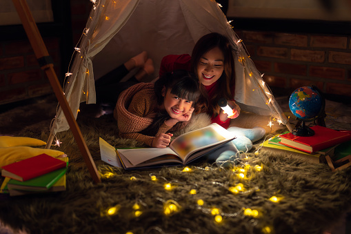 Asian Mother and daughter relax with tent and light in they bed room and read a teblet togather on night time at home