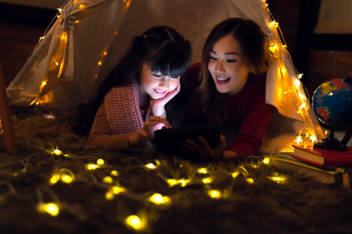 Asian Mother and daughter relax with tent and light in they bed room and read a teblet togather on night time at home