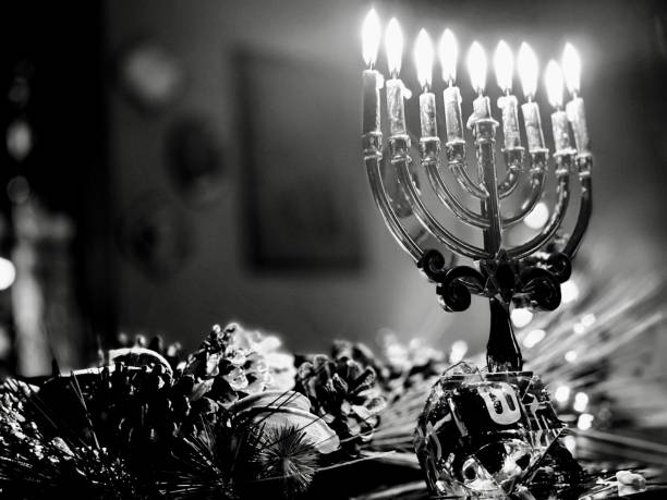 Monochromatic image of lighted Menorah. Tabletop centerpiece decorated with pine cones and dried fruit. Crystal dreidel with Hebrew script. Religious symbol celebrating the miracle of light and the story of the Macabees. Defocused background with space for copy.