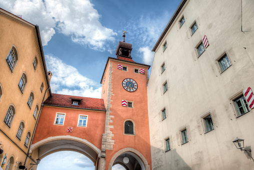 Ensemble of buildings with gate, archway and tower with clock on the Danube in the historic old town of Regensburg in oblique lower view