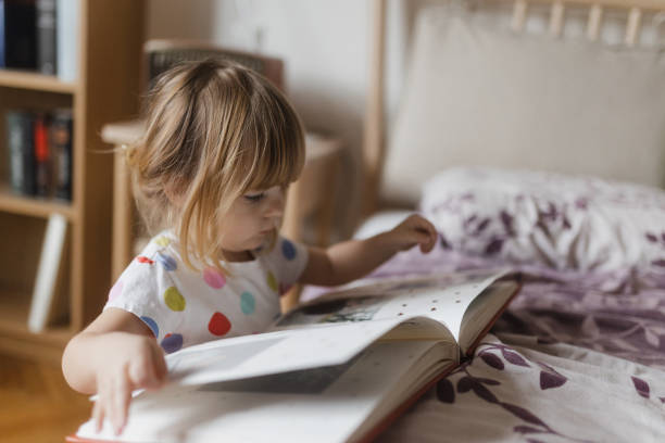 istock Cute little girl reading book lying on bed. 1524441817