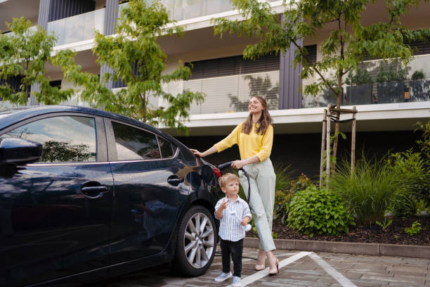 Smiling mother and her little son charging their electric car on the street. stock photo
