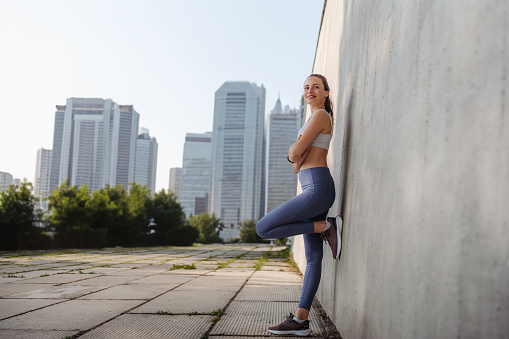 Side view of young sporty woman in sportswear excercising outdoors. Fitness woman in front of concrete wall in the city. Healthy lifestyle concept. Street workout.