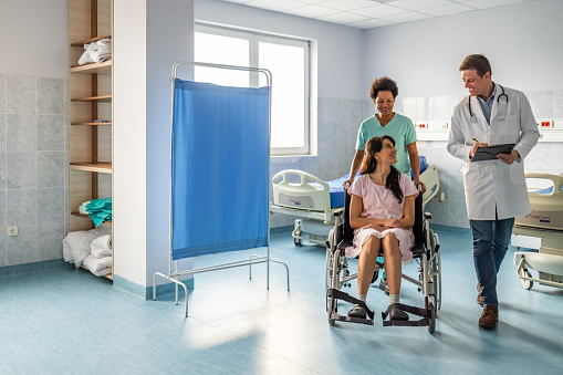 Male doctor discussing with woman sitting on wheelchair in hospital ward