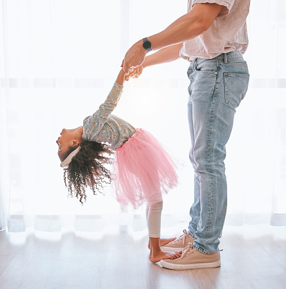Happy, bonding and father teaching child to dance on feet with support holding hands in their house. Help, ballerina and dancing girl learning a move with her dad in the living room of family home