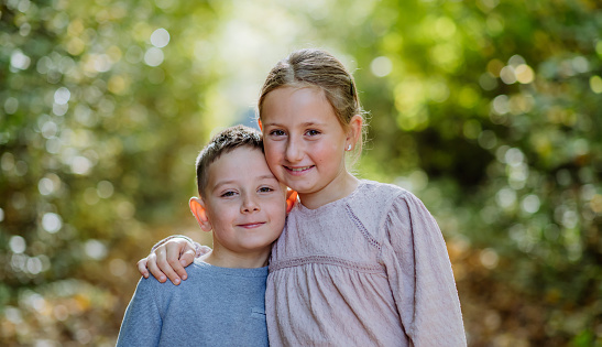 Portrait of little children, siblings, hugging in a forest.