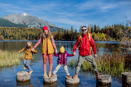 Happy young family with two little children, standing on wooden steps on the shore of the lake in mountains.