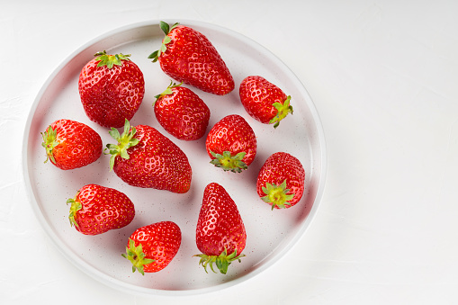 Ripe strawberries on white plate. Fresh delicious strawberries on white background. Top view. Copy space