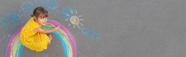 un bambino disegna un arcobaleno sull'asfalto. messa a fuoco selettiva. - little girls sidewalk child chalk foto e immagini stock
