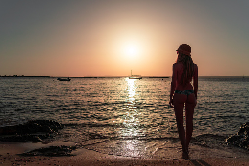 Rear view of blonde woman with hat Golden sunset on calm Mediterranean Sea. Nautical vessel in the sea