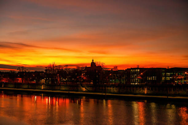 Colorful bright sunset over Vistula river in Krakow, Poland. Black silhouettes of houses, churches, office buildings, boulevard and reflect in water against orange hot sunset sky