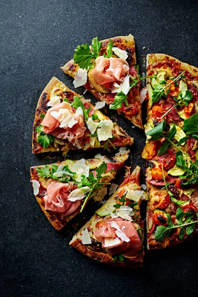 Photo of Pizza topped with serrano ham, arugula and grana padano cheese. Top view.