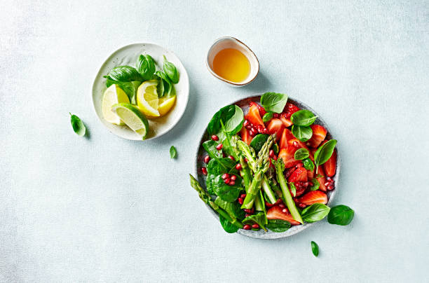 Spring salad with strawberries, pomegranate, asparagus, spinach, basil leaves and citrus-honey dressing. Top view stock photo