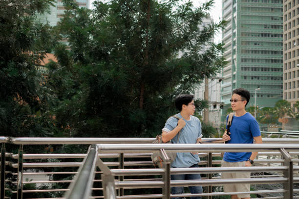 istock Asian handsome man and LGBTer standing on overpass, talking with enjoyment, tree and skyscaper background. Traveling in city. 1524919040