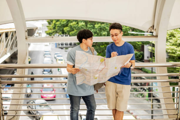 istock Asian handsome mand and LGBTER looking map and talking about destination on overpass with blur city road background and bridge to sky train. 1524919560