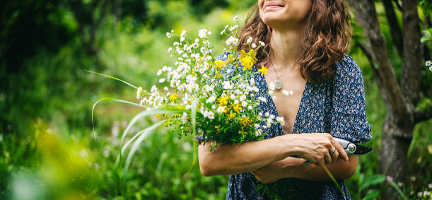 Young cheerful smiling woman in summer dress holding a bouquet of wildflowers