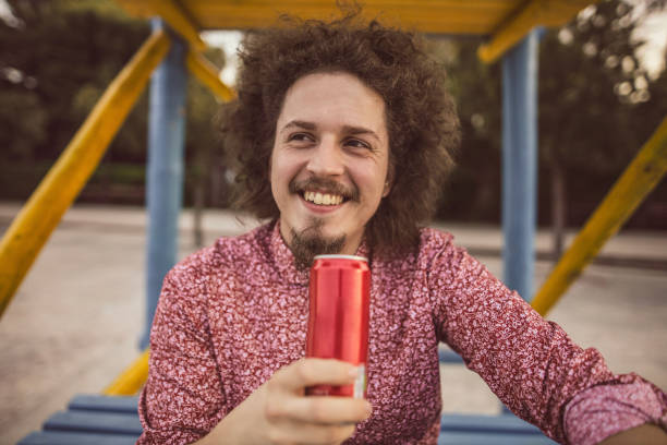 Joyful boy drinking lemonade from a glass bottle against a beautiful sky backdrop. He wears a plaid shirt and a backpack. Vibrant colors
