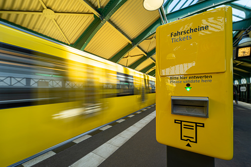 Close up of yellow ticket validator at subway station against leaving subway train, Berlin Prenzlauer Berg Eberswalter Strasse