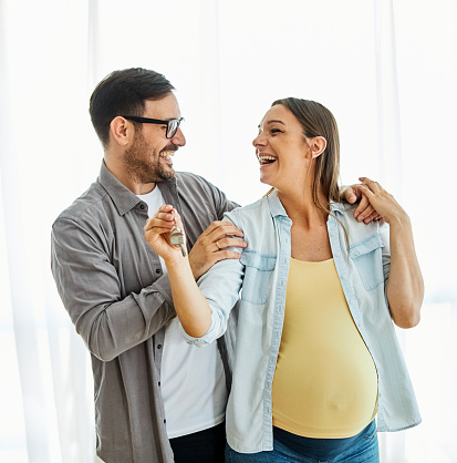 Happy young couple, pregnant woman,  buying a new house and holding the keys
