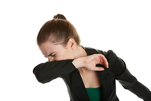 A young business woman, sneezing into her sleeve to prevent spreading germs.  Shot on white background.