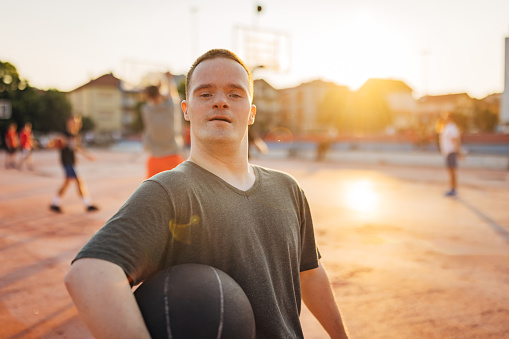 Waist up view of an active man with Down syndrome holding a basketball in his hands and looking directly at the camera while standing on a basketball court