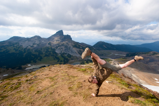 Young man at the peak of the mountain upside down doing a hand-stall overlooking another mountain peak.