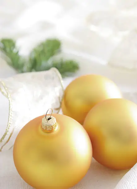 Closeup on yellow glass balls. White transparent ribbon and fir tree branch in background. All on white table cloth