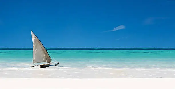 Sail boat in the sea beside the beach with clear blue sky and white sand