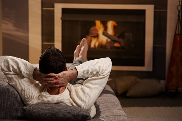 A man relaxing with his feet up on a sofa by the fire stock photo