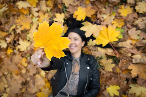 Beautiful smiling woman outdoor portrait holding a leaf in front of the camera.