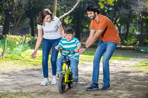 Indian mother and father helping son learn to ride a bicycle in the park outdoor. kid having fun with bike while mom and dad helping him balance. family together enjoy holiday and spend time together